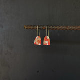 Pair of orange and white patterned earrings hanging on a dark background
