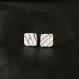 Pair of square-shaped earrings with blue and white marbled pattern on a dark surface