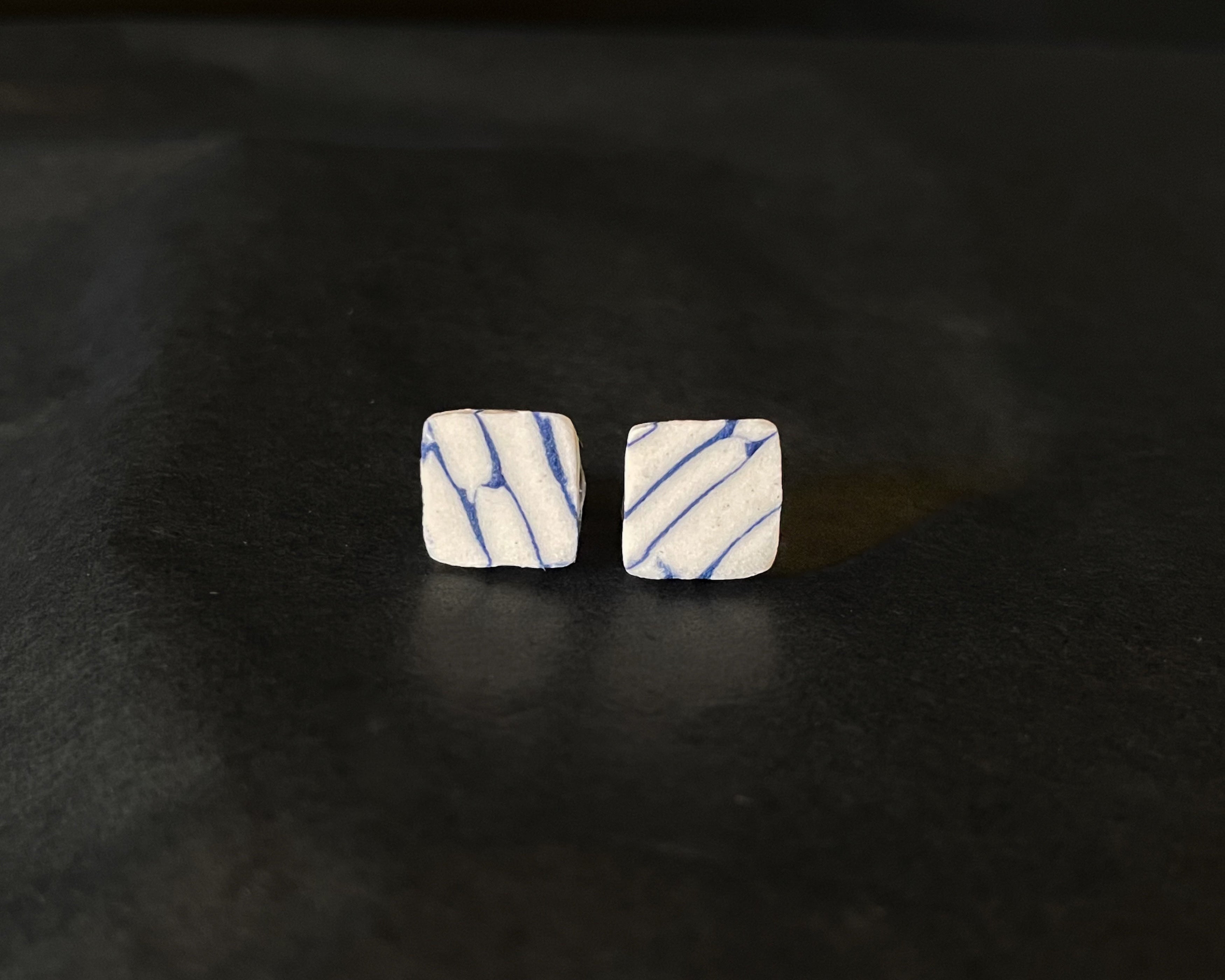 Pair of square-shaped earrings with blue and white marbled pattern on a dark surface