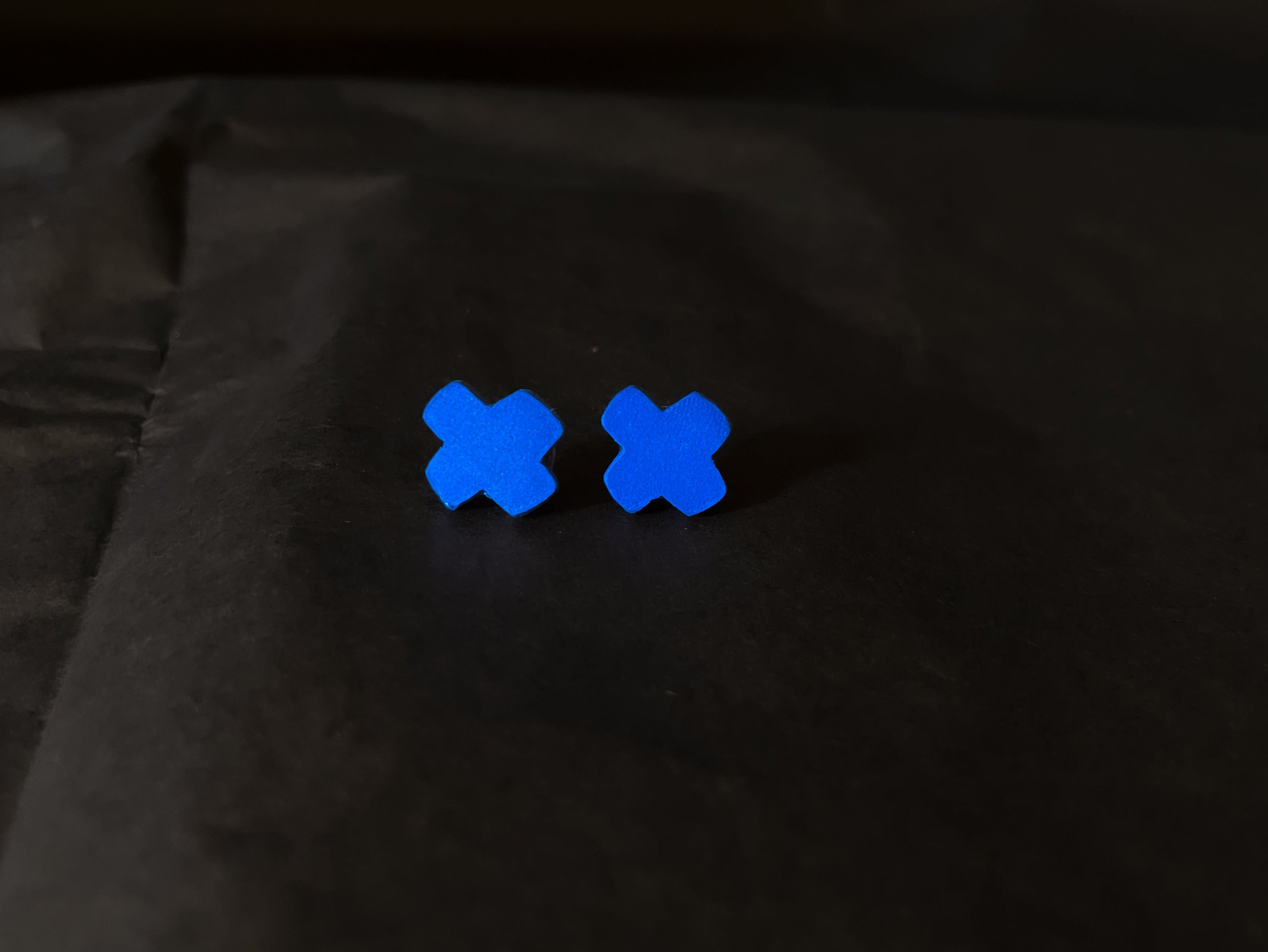 Two blue 'X' stud earrings on a black background