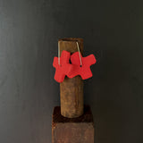 Red x-shaped earrings hanging on a rusty metal rod against a dark background