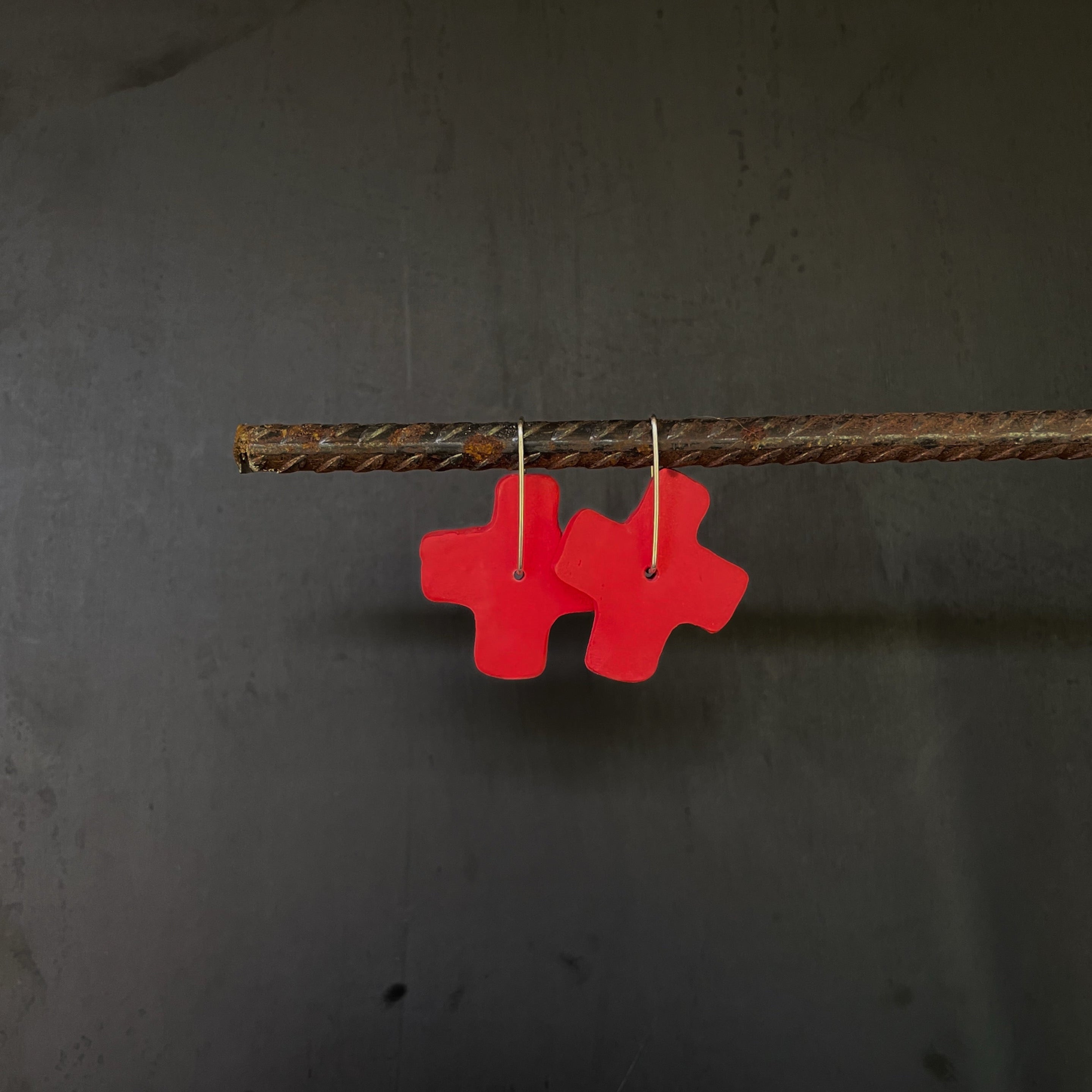 Red x-shaped earrings hanging on a dark background