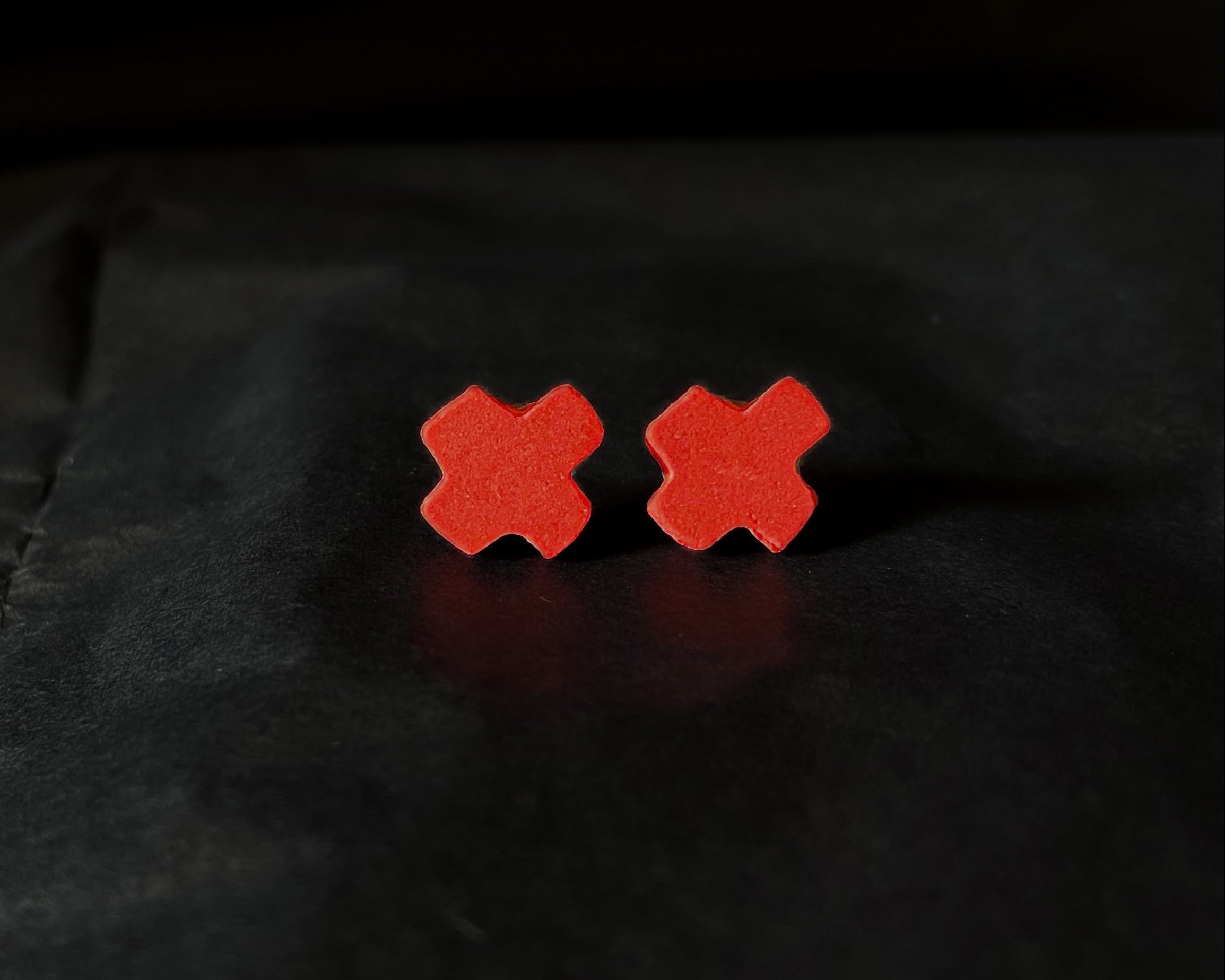 Red X-shaped earrings on a black background