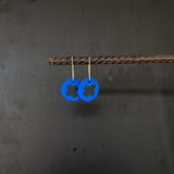 Blue circular earrings with black x design on a dark gray background