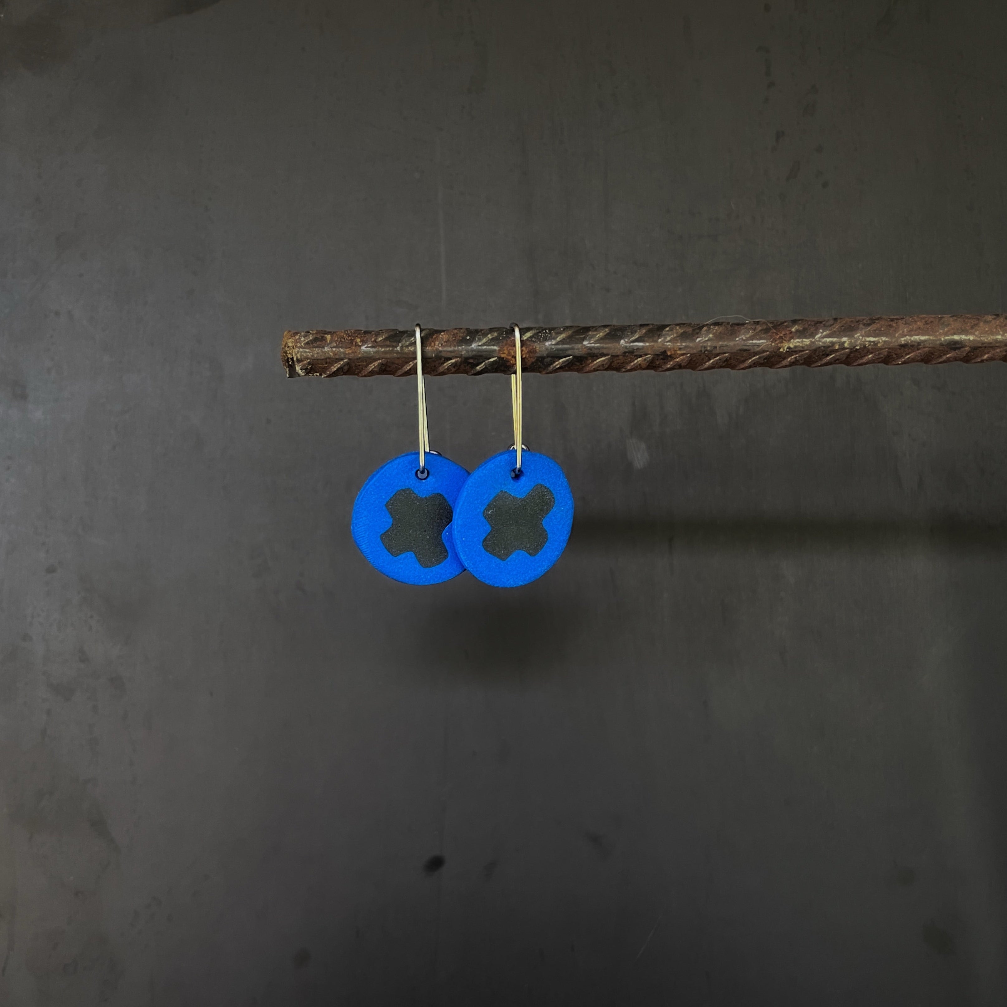 Blue circular earrings with black x design on a dark gray background