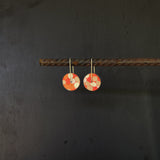 Pair of coral orange earrings with circular designs hanging on a dark background