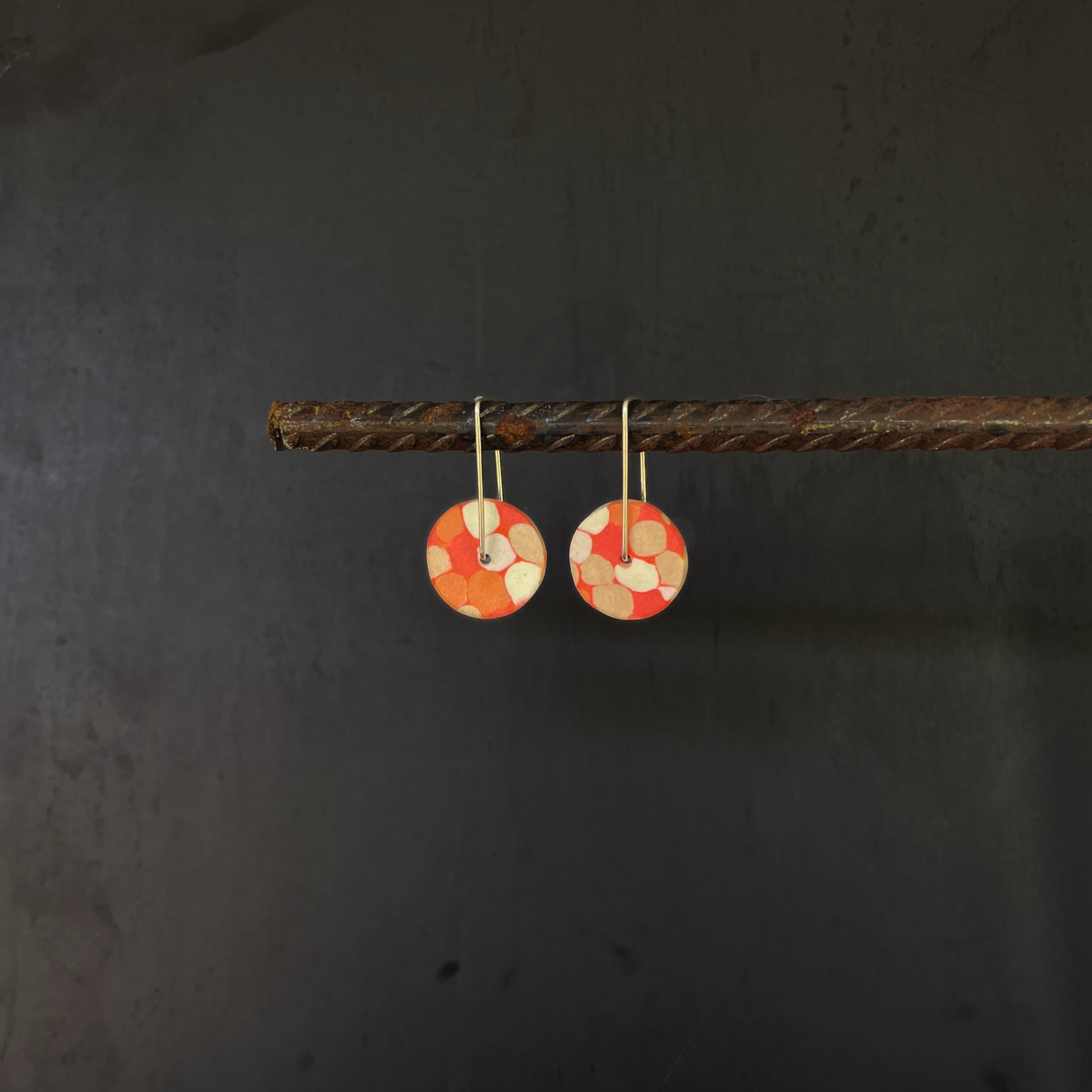Pair of coral orange earrings with circular designs hanging on a dark background